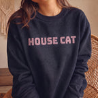 Woman modeling dark navy HOUSE CAT sweatshirt with raised puff print lettering, cozy graphic cat crewneck designed for cat lovers and everyday wear.