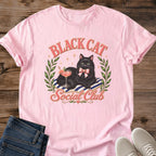 Black Cat Shirt Women Graphic Tee Design Luxurious Cat Green Eyes Detail Pink Cocktail Glass Lifestyle Imagery Striped Cushion Pink Bow Accent Olive Wreath Frame Cat Lover Gift Perfect Coquette Style Fashion Feminine Aesthetic Casual Wear