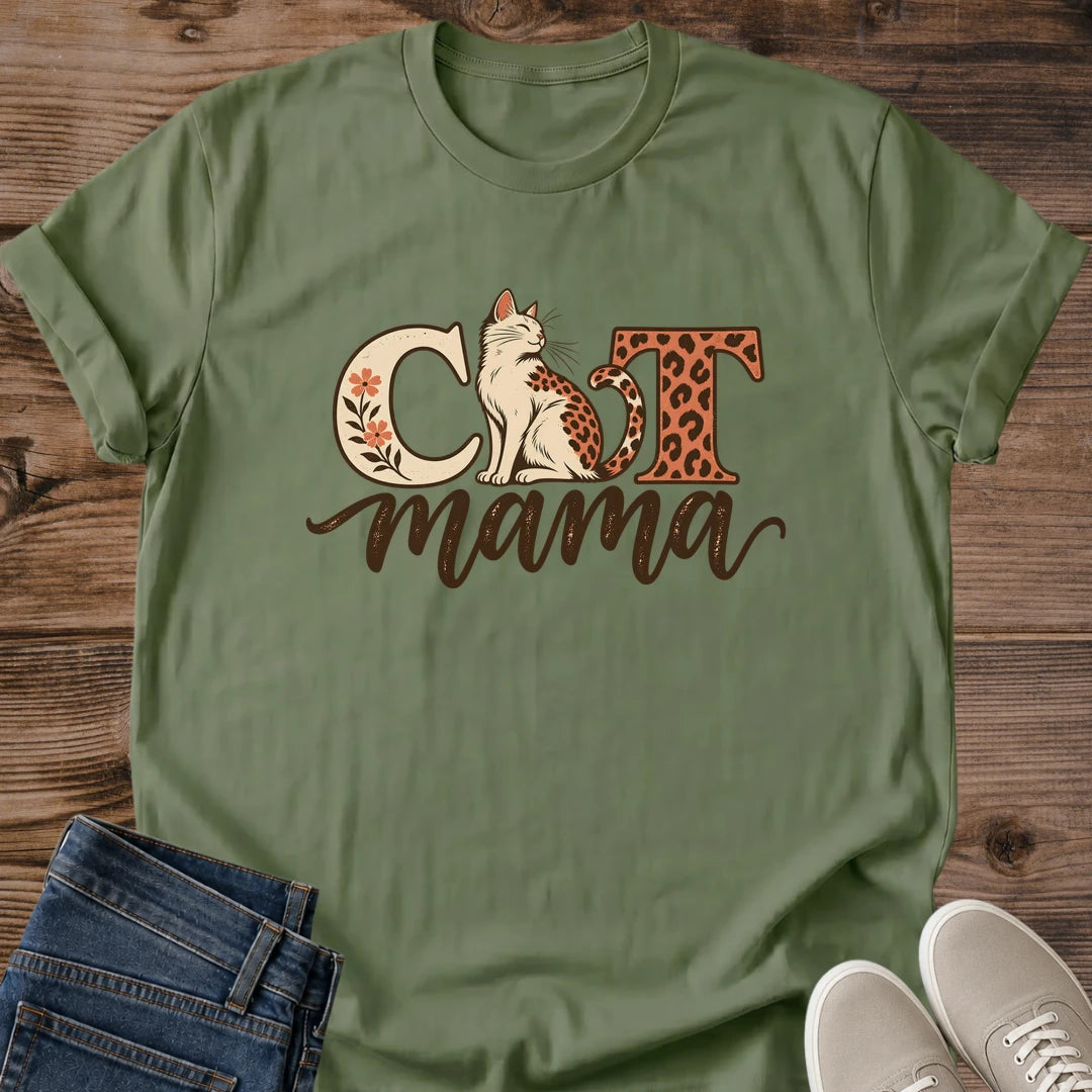 Military green Cat Mama T-shirt flat lay with a seated leopard-spotted cat, cream floral C, rust leopard-print T and brown mama script.