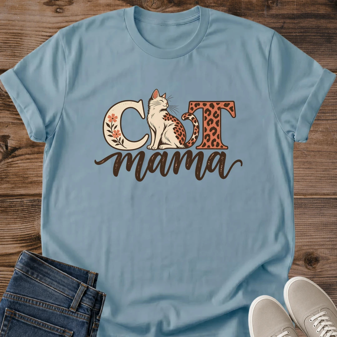 Stone blue Cat Mama T-shirt flat lay with a seated leopard-spotted cat between floral and animal-print letters, above brown script mama.