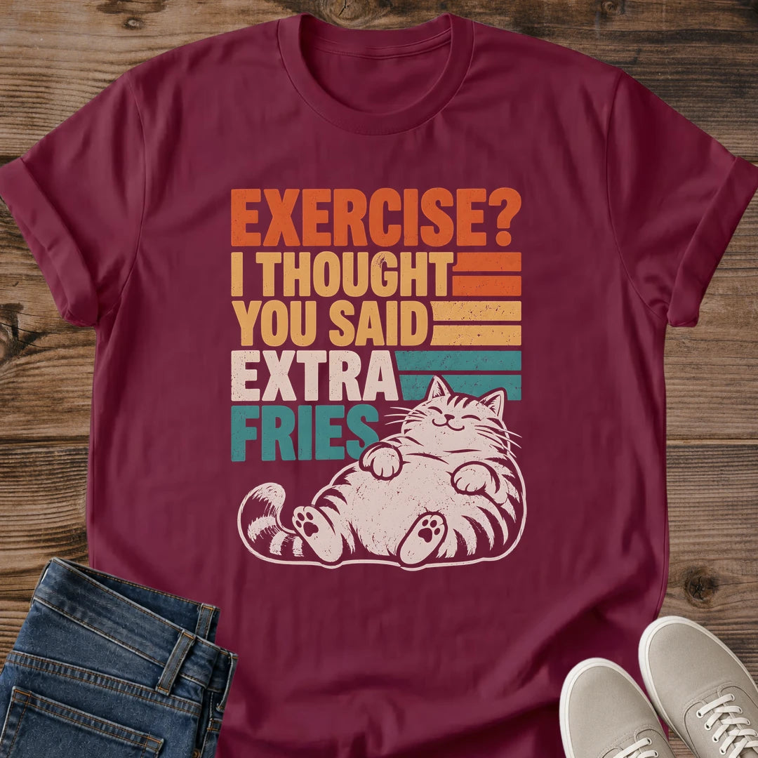 Maroon Gildan 64000 unisex Extra Fries cat T-shirt laid flat on rustic wood, with a crew neckline, rolled short sleeves, folded blue jeans and light gray lace-up sneakers. The distressed chest graphic combines orange, yellow, cream and teal stripes with the slogan "EXERCISE? I THOUGHT YOU SAID EXTRA FRIES." A cream striped tabby reclines beneath the stacked lettering, eyes closed, front paws resting on its belly and hind paws facing forward.