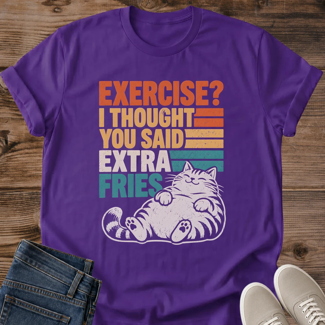Purple Gildan 64000 unisex funny cat T-shirt shown in a front flat lay on wooden planks with rolled short sleeves. The vintage-style print reads "EXERCISE? I THOUGHT YOU SAID EXTRA FRIES" in orange, yellow, cream and teal block letters beside horizontal stripes. A cream-colored lounging tabby with closed eyes, a round belly and visible hind paw pads completes the distressed design. Folded blue jeans and light gray sneakers frame the lower corners.