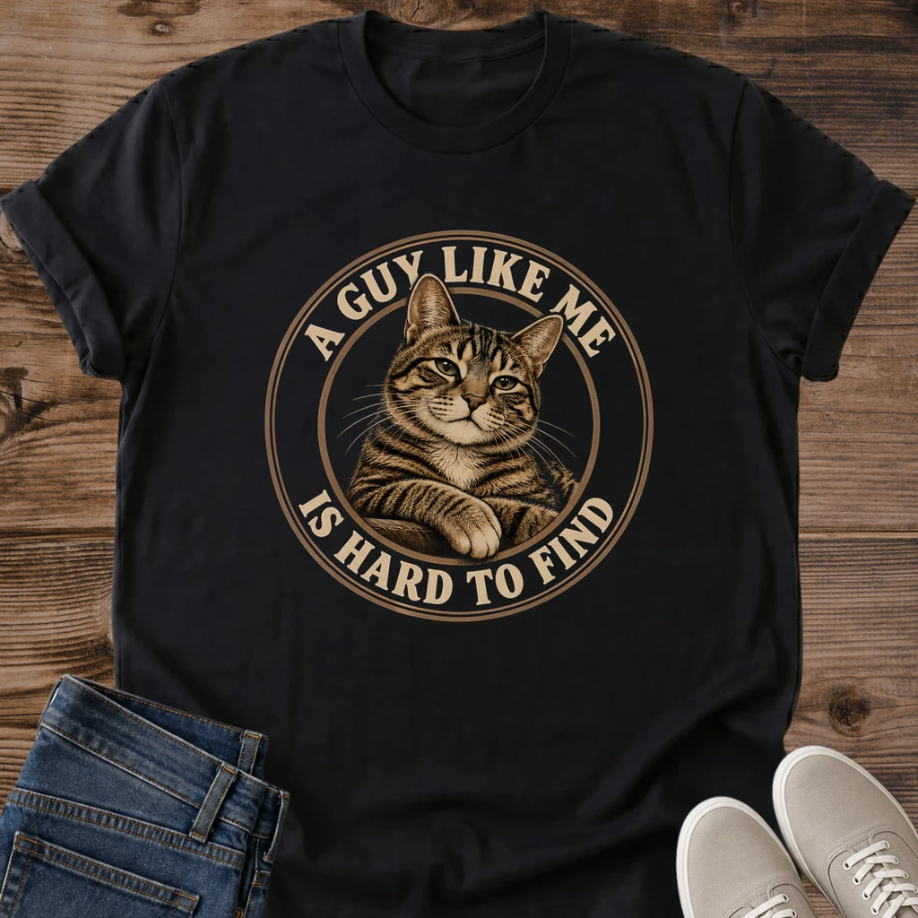 Black T-shirt flat lay featuring a brown tabby with crossed front paws inside a tan circular border reading A Guy Like Me Is Hard to Find.