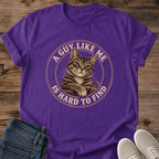 Purple T-shirt flat lay featuring a brown tabby with crossed front paws inside a tan circular border reading A Guy Like Me Is Hard to Find.