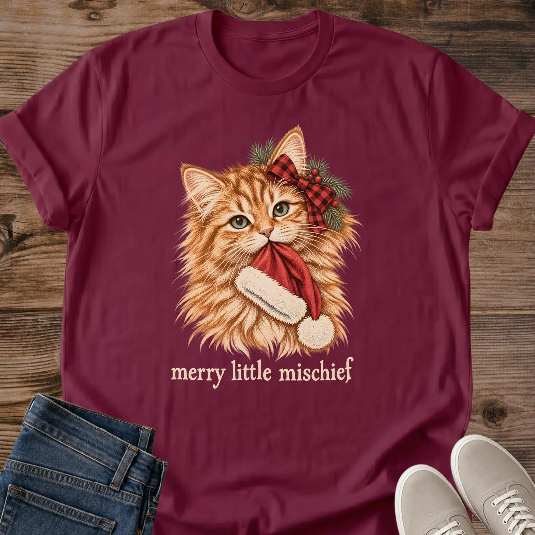 Maroon Merry Little Mischief Christmas cat T-shirt flat lay featuring an orange tabby with a red plaid bow holding a Santa hat.
