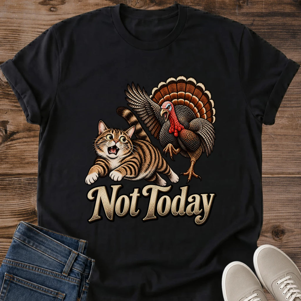 Black Gildan 64000 unisex Thanksgiving cat T-shirt laid flat on wooden planks with rolled short sleeves, folded blue jeans and light gray lace-up sneakers. The vintage chest artwork shows a startled brown tabby running from a turkey with raised wings and a fanned orange-brown tail. Large cream "Not Today" lettering beneath the animals stands out against the black fabric.