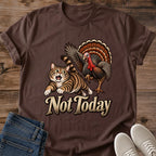 Dark Chocolate brown Gildan 64000 unisex Thanksgiving cat T-shirt in a front-view flat lay on wooden planks, styled with folded blue jeans and light gray sneakers. The crewneck tee has rolled sleeves and a vintage illustration of a startled striped tabby fleeing a turkey with spread wings, orange-brown tail feathers and a red wattle, above large cream "Not Today" lettering.