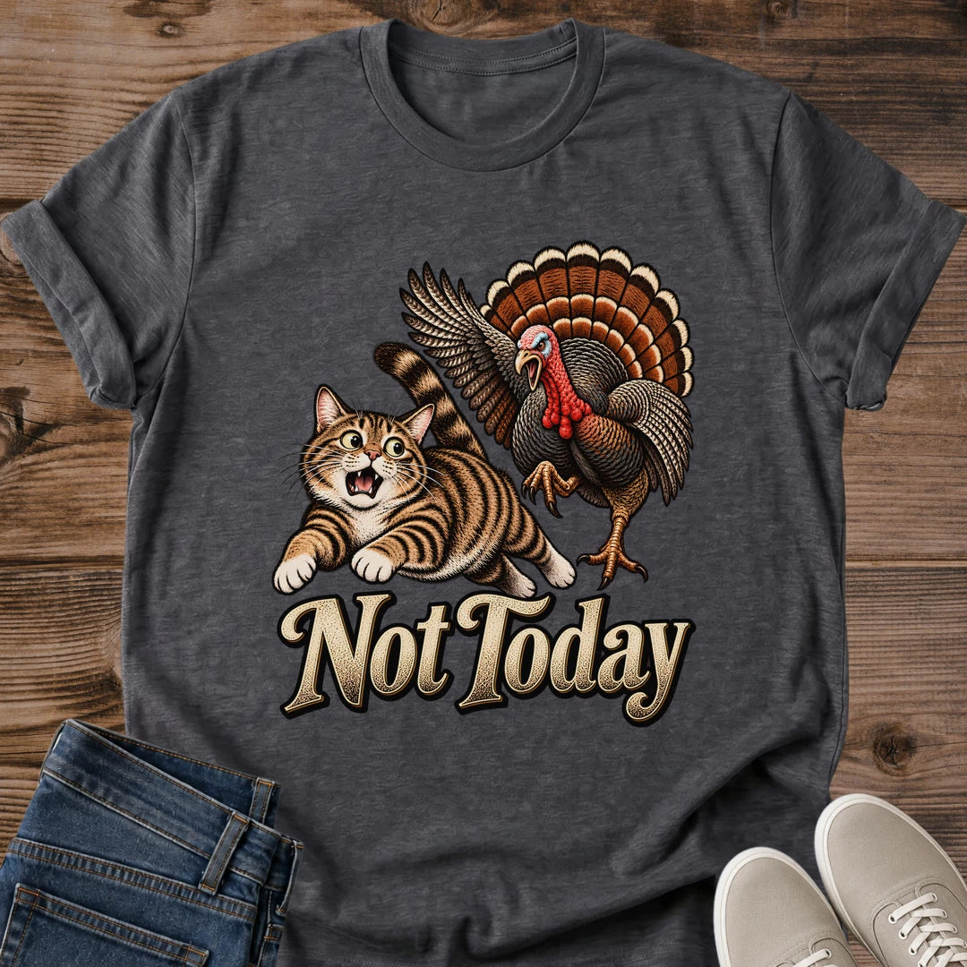 Dark Heather charcoal gray Gildan 64000 unisex Thanksgiving cat T-shirt in a flat lay on rustic wood with folded blue jeans and light gray sneakers. The heathered crewneck tee has rolled sleeves and a vintage chest print of a startled brown tabby fleeing a turkey with raised wings, a red wattle and a fanned orange-brown tail, above cream "Not Today" lettering with dark outlines.