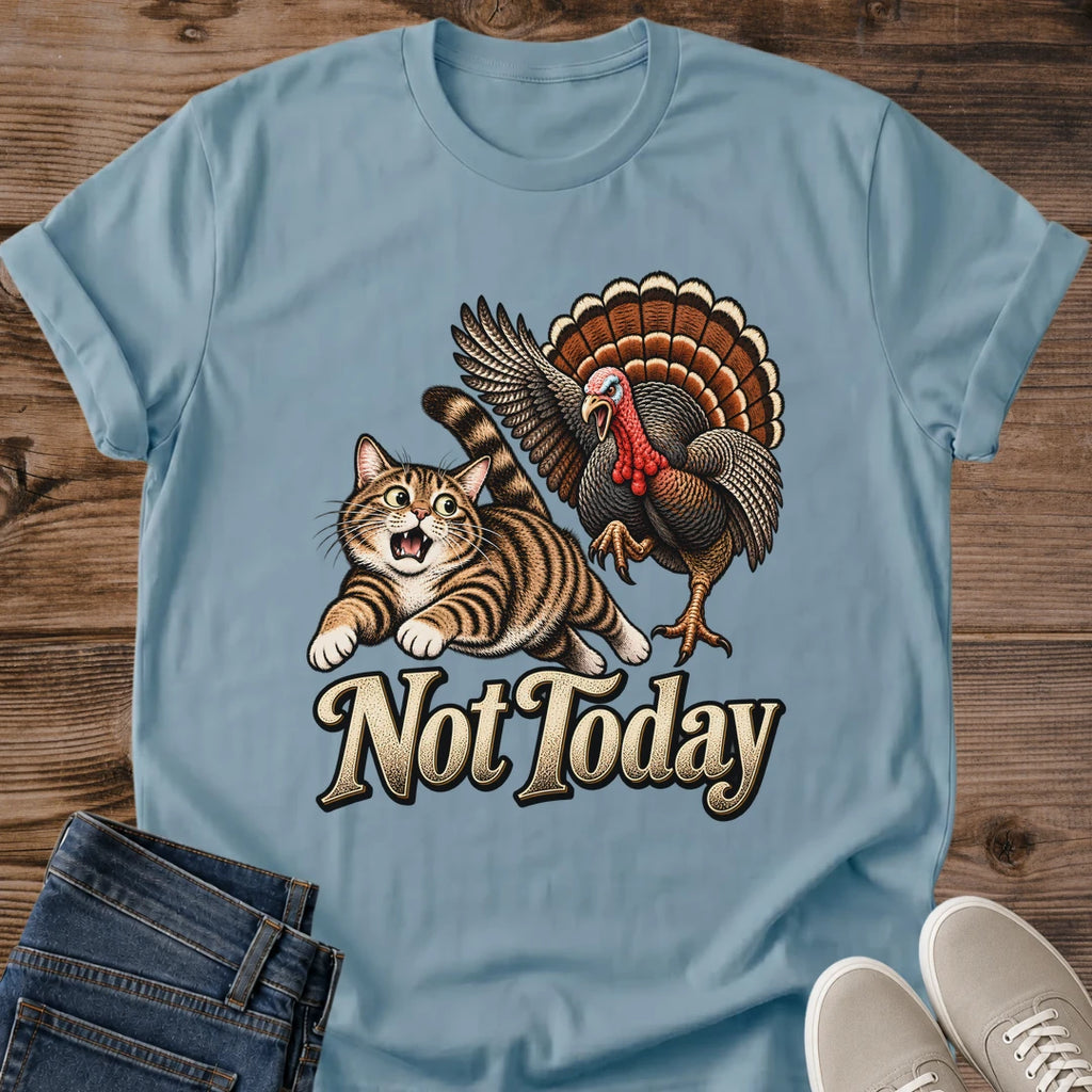 Stone Blue Gildan 64000 unisex Thanksgiving cat T-shirt laid flat on rustic wood, with a crew neckline and rolled short sleeves. A brown striped tabby with an open mouth runs ahead of a turkey with raised wings and a fan of orange-brown feathers; cream "Not Today" lettering sits below the vintage graphic. Folded blue jeans and light gray lace-up sneakers frame the lower corners.