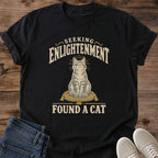 Vintage Style Cat Tee Spiritual Humor Graphic Shirt Seeking Enlightenment Design Funny Cat Lover Gift Lightweight Cotton Fabric Comfortable Casual Wear Muted Warm Tones Dark Background Centered Cat Illustration Quirky Novelty Shirt Everyday