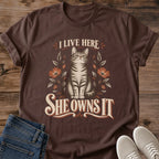 Funny Cat Graphic Tee I Live Here She Owns It Floral Print Vintage Aesthetic Cat Owner Shirt Gift For Cat Lovers Softstyle Cotton Comfortable Relaxed Fit Statement Piece Everyday Casual Wear Apparel Gift Idea For All