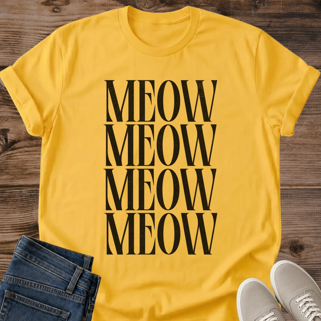 Daisy yellow Gildan 64000 unisex Stacked Meow cat T-shirt in a front-view flat lay on wooden planks. Four rows of tall black uppercase serif letters spell "MEOW" down the center, creating a bold rectangular typography design against the bright yellow fabric. The crewneck shirt has rolled short sleeves, with folded dark blue jeans and light gray lace-up sneakers framing the bottom.