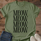 Military Green olive Gildan 64000 unisex Stacked Meow cat T-shirt laid flat on rustic wood with the front print fully visible. "MEOW" repeats in four tightly stacked rows of tall black uppercase serif letters across the center of the olive green shirt. A round crew neck, rolled short sleeves, folded dark blue jeans and light gray lace-up sneakers complete the mockup.