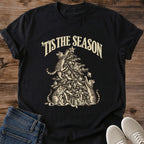 Black 'Tis the Season Christmas cat T-shirt flat lay with cream vintage-style artwork of cats climbing and playing in a decorated tree above gifts.