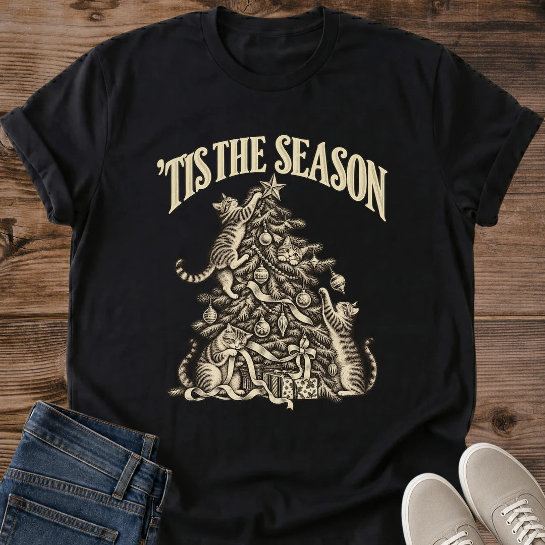 Black 'Tis the Season Christmas cat T-shirt flat lay with cream vintage-style artwork of cats climbing and playing in a decorated tree above gifts.