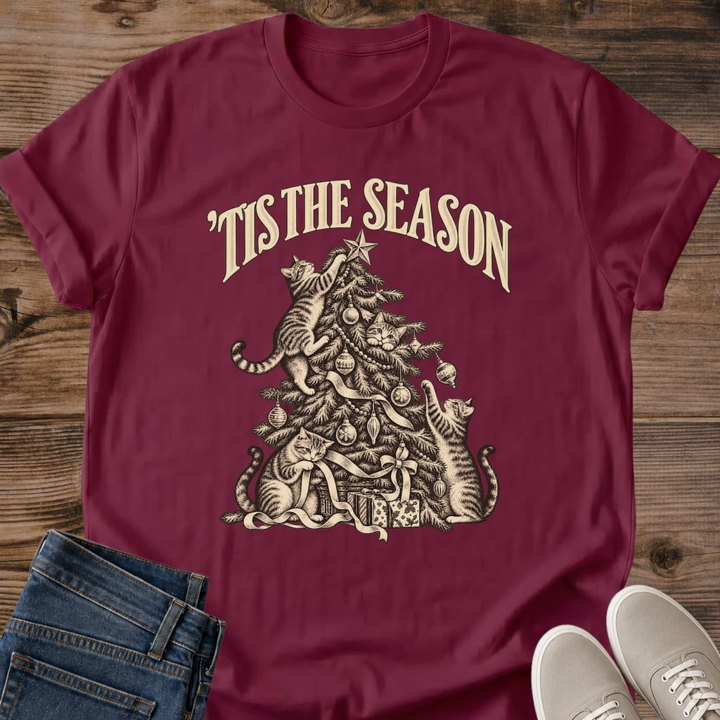Maroon 'Tis the Season Christmas cat T-shirt flat lay with cream vintage-style artwork of cats climbing and playing in a decorated tree above gifts.