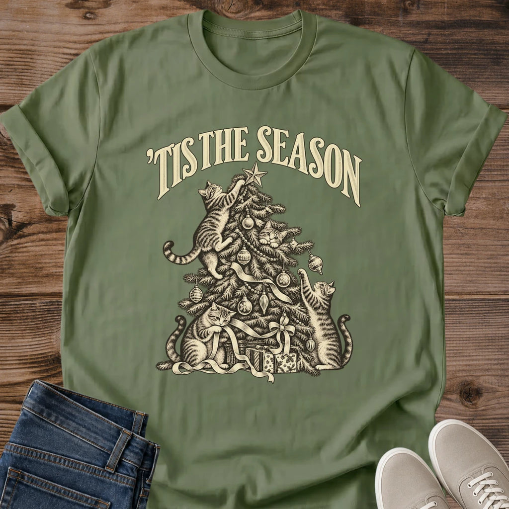 Military Green 'Tis the Season Christmas cat T-shirt flat lay with cream vintage-style artwork of cats climbing and playing in a decorated tree above gifts.