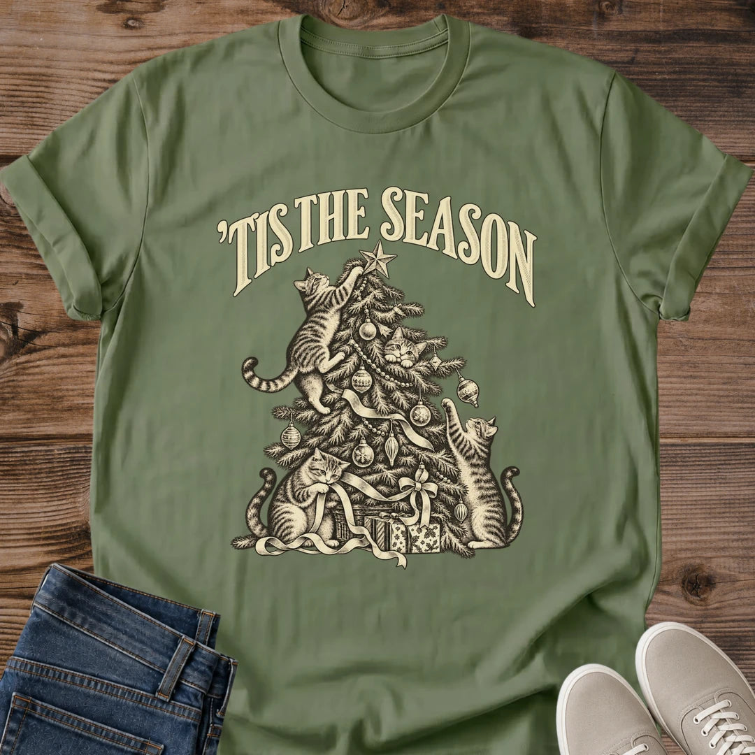 Military Green 'Tis the Season Christmas cat T-shirt flat lay with cream vintage-style artwork of cats climbing and playing in a decorated tree above gifts.